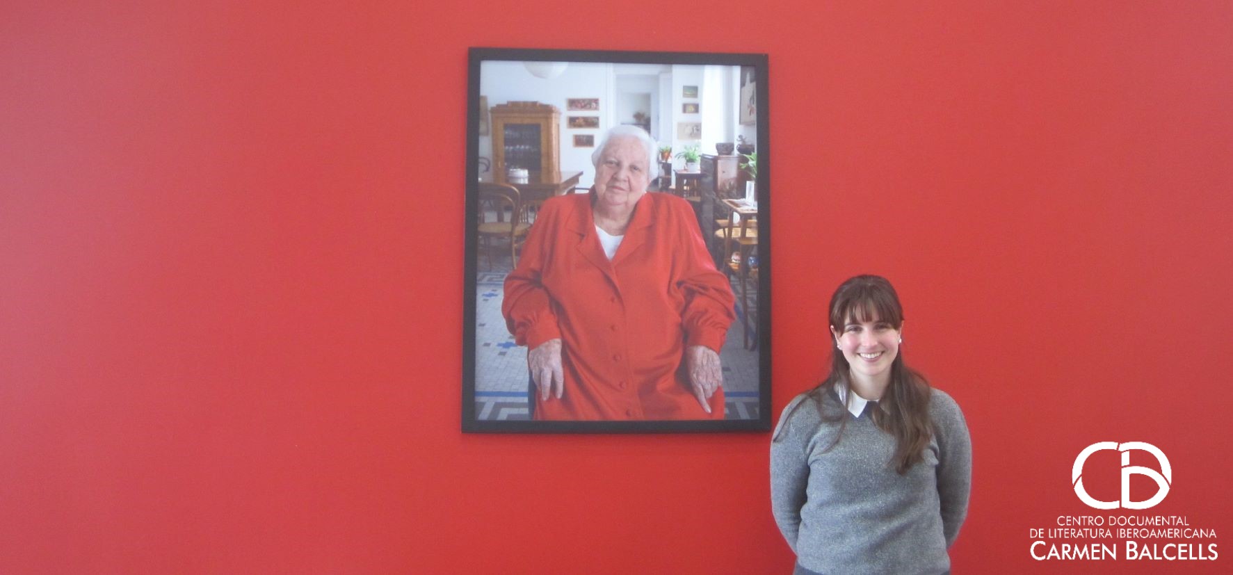 Dominique Lear parada ante el muro rojo del centro documental junto al retrato de Carmen Balcells